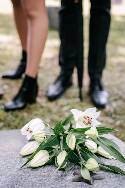 A close-up of a floral arrangement featuring white lilies with their large, trumpet-shaped petals and prominent stamens, accompanied by unopened white lily buds and lush green leaves. The bouquet is r
