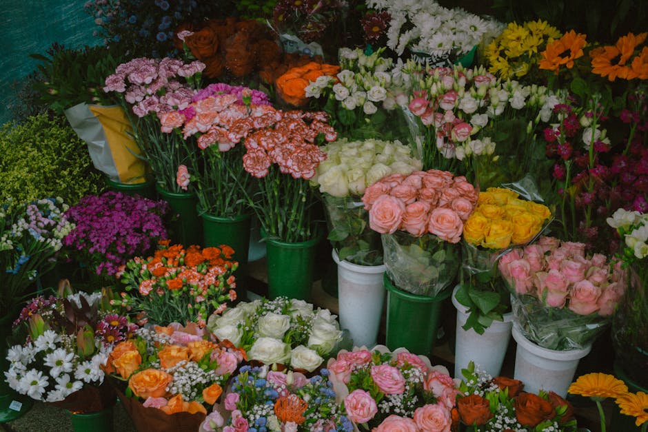A vibrant display of fresh floral arrangements at a flower shop, featuring a variety of flowers including pink and white roses, orange and yellow roses, purple chrysanthemums, and white daisies. The f