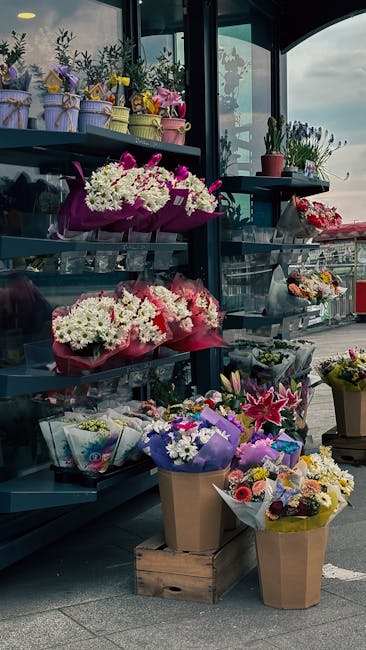 A display of fresh floral arrangements and bouquets on black metal shelves outside Wallington Florist, located under a glass canopy with a view of the street. The arrangements include white, pink, pur